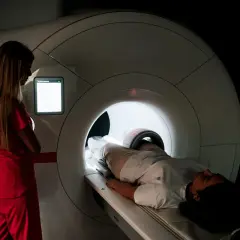 Pacjentka leży w aparacie do rezonansu magnetycznego. Lekarka w czerwonym stroju nadzoruje badanie, decydując, czy wykonać rezonans z kontrastem czy bez.
