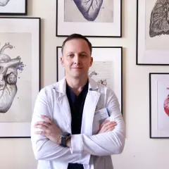 Dr nauk medycznych, lekarz kardiolog, stoi na tle obrazów z sercami.