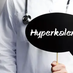 Lekarz w białym fartuchu ze stetoskopem trzyma czarną chmurkę z napisem "Hyperkalemia". Oznacza to podwyższony potas we krwi.