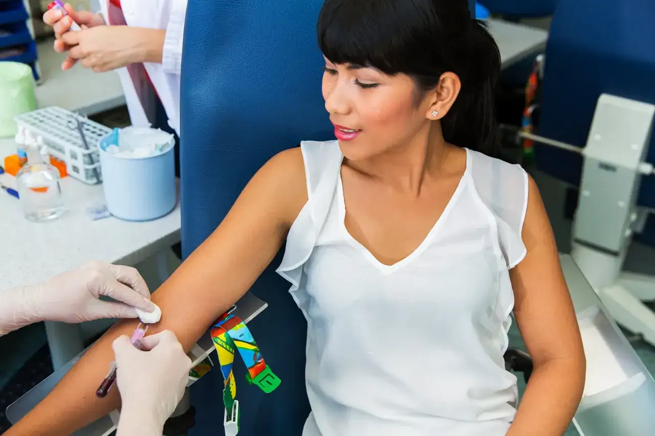 Kobieta w białej bluzce poddaje się pobraniu krwi, co może pomóc w diagnostyce zaburzeń metabolicznych.
